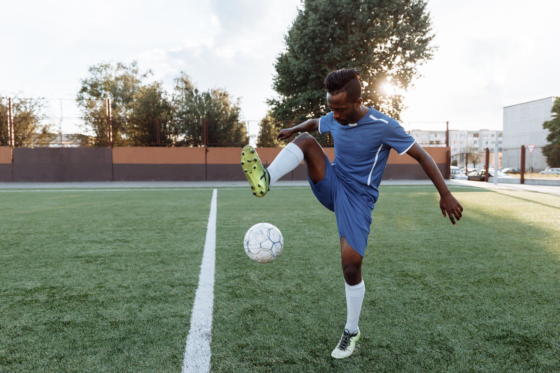 Soccer player in blue uniform juggling a ball on a field at sunset