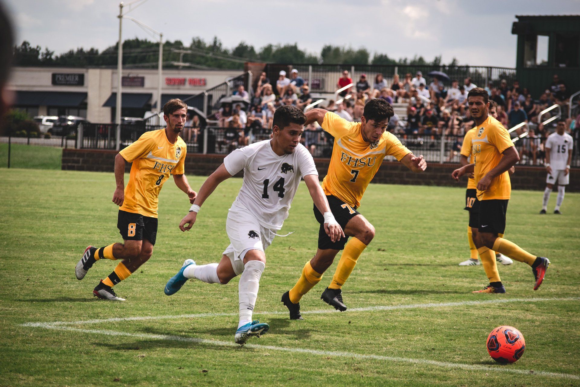 Soccer match with players in white and yellow battling for the ball on a grassy field