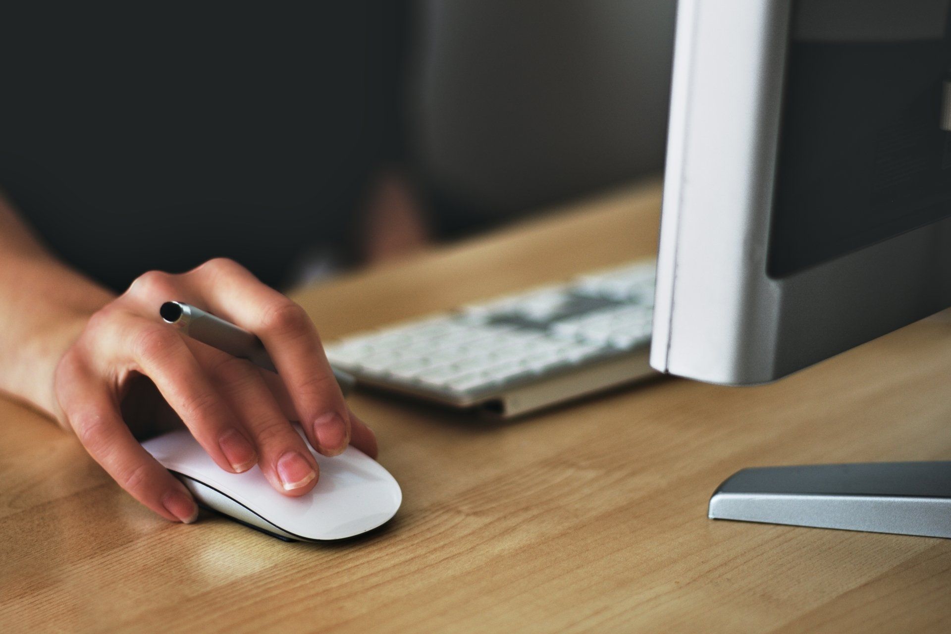 Hand using a white mouse on a desk beside a keyboard and monitor