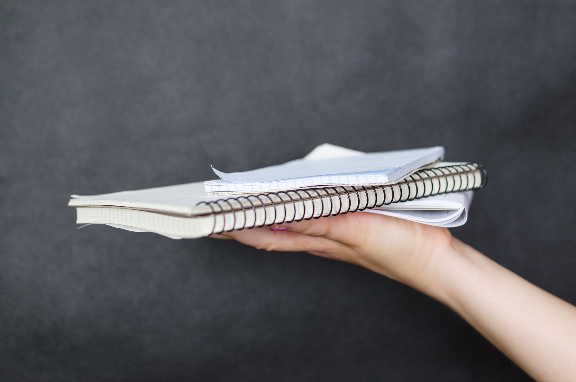 Hand holding a stack of spiral notebooks against a gray background