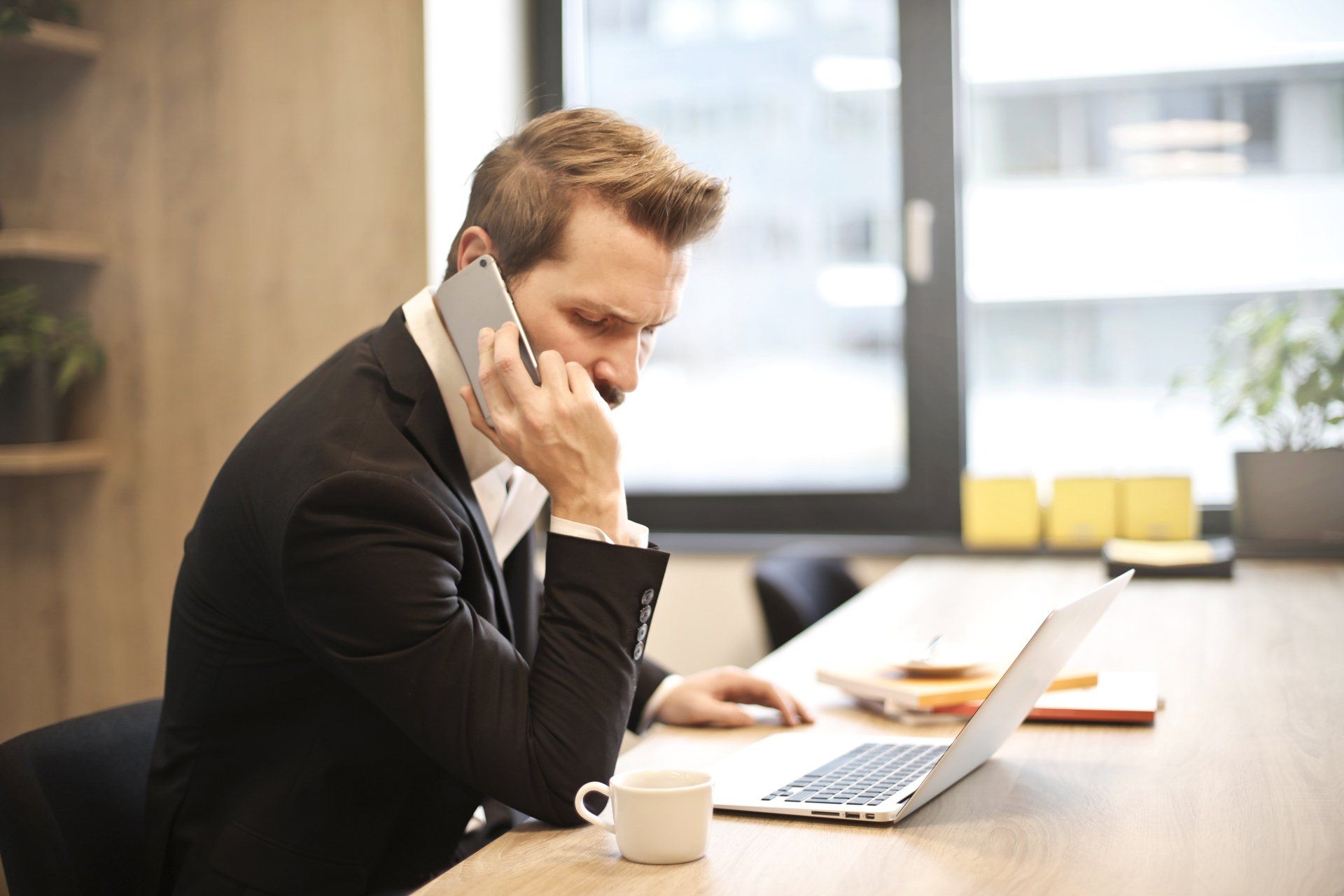 Person on a phone call at a desk, working on a laptop in a bright office