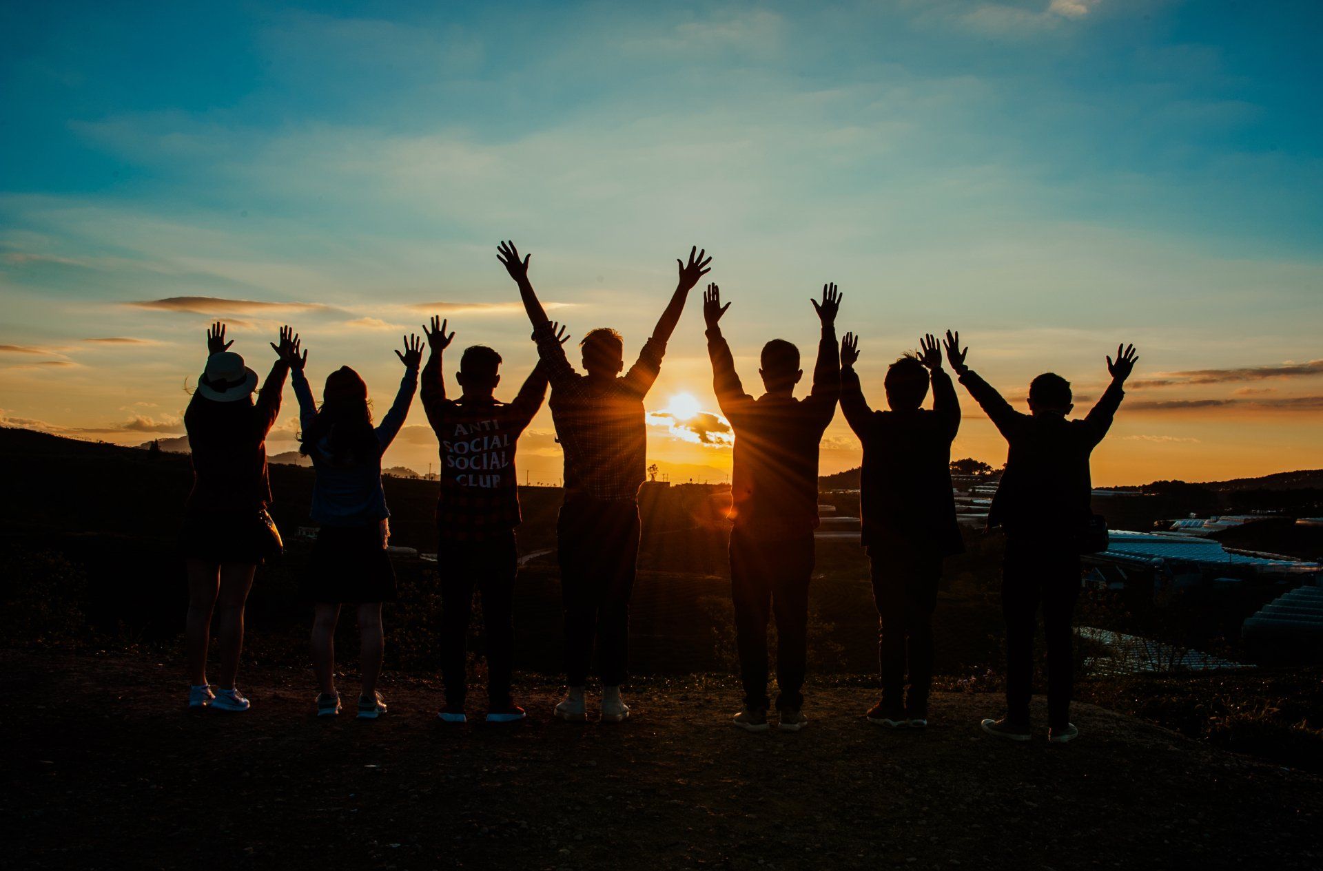 Silhouetted group of people with raised arms at sunset on a hilltop by the water