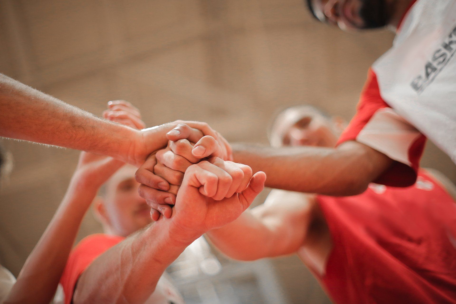 Hands stacked together in a team huddle, with players wearing red and white jerseys.